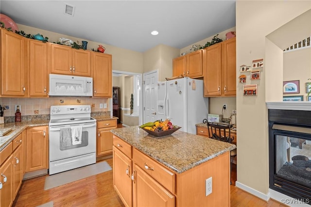 kitchen featuring white appliances, light hardwood / wood-style flooring, light stone countertops, and a kitchen island