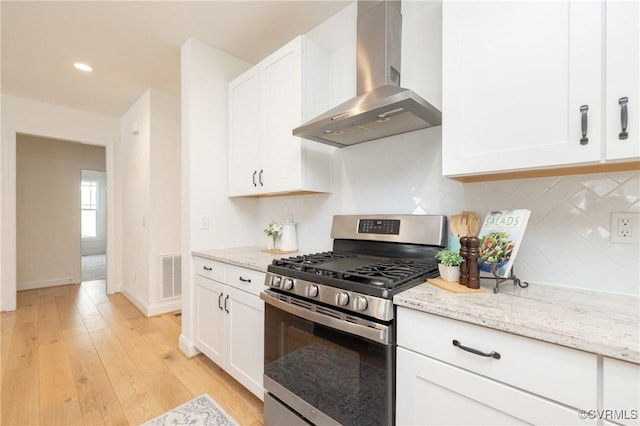 kitchen with backsplash, white cabinets, light stone counters, gas stove, and wall chimney exhaust hood