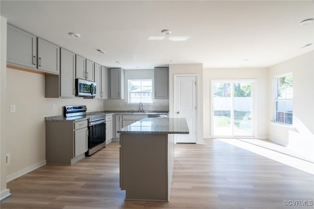 kitchen featuring gray cabinets, stone counters, stainless steel appliances, a center island, and light hardwood / wood-style floors