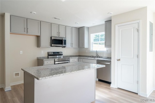 kitchen with appliances with stainless steel finishes, light stone countertops, a kitchen island, and light wood-type flooring