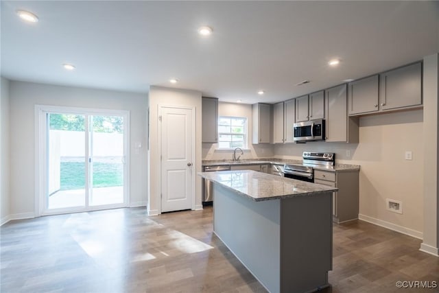 kitchen featuring a center island, light hardwood / wood-style flooring, gray cabinets, stainless steel appliances, and light stone countertops