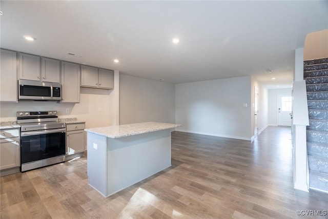 kitchen with a kitchen island, gray cabinetry, stainless steel appliances, light stone countertops, and light wood-type flooring