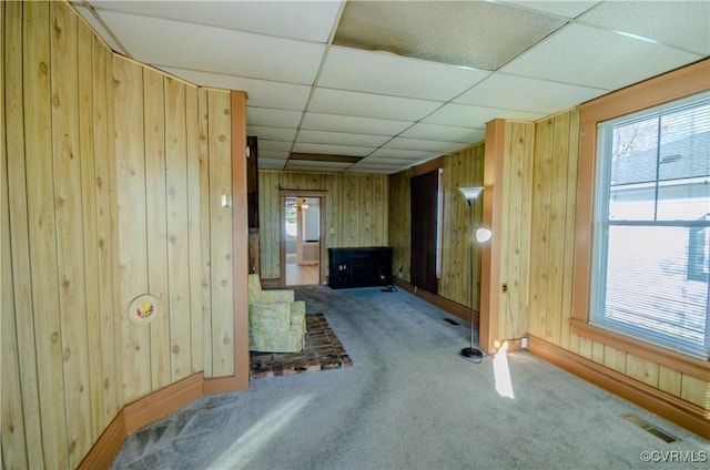 unfurnished room with carpet, a drop ceiling, and wooden walls