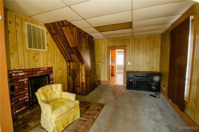 living area with a paneled ceiling, dark carpet, and a brick fireplace