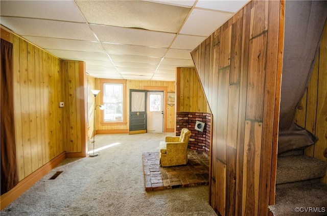 living area featuring carpet floors, a drop ceiling, and wooden walls