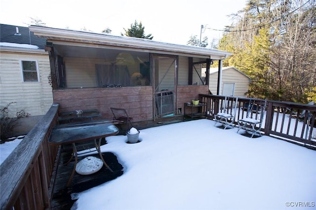 snow covered rear of property featuring a storage shed and a wooden deck