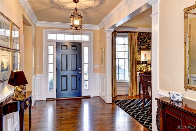 foyer entrance featuring a wainscoted wall, dark wood finished floors, a decorative wall, ornamental molding, and ornate columns