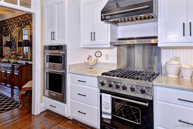 kitchen featuring white cabinets, dark wood finished floors, light stone countertops, stainless steel appliances, and wall chimney range hood