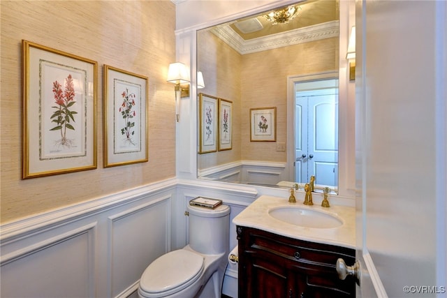 half bathroom with a wainscoted wall, toilet, vanity, and a decorative wall