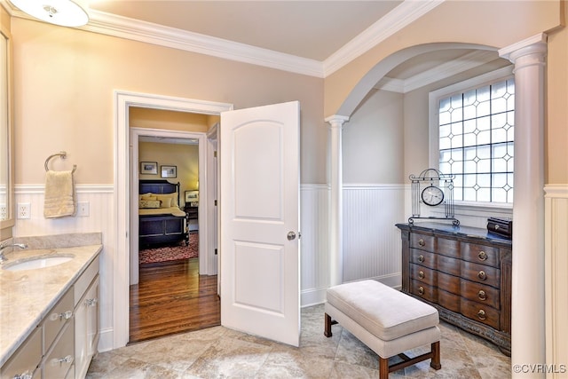 bathroom featuring ornate columns, vanity, crown molding, and wainscoting