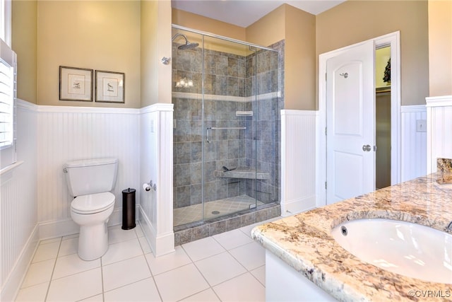 bathroom with toilet, a wainscoted wall, vanity, a shower stall, and tile patterned floors