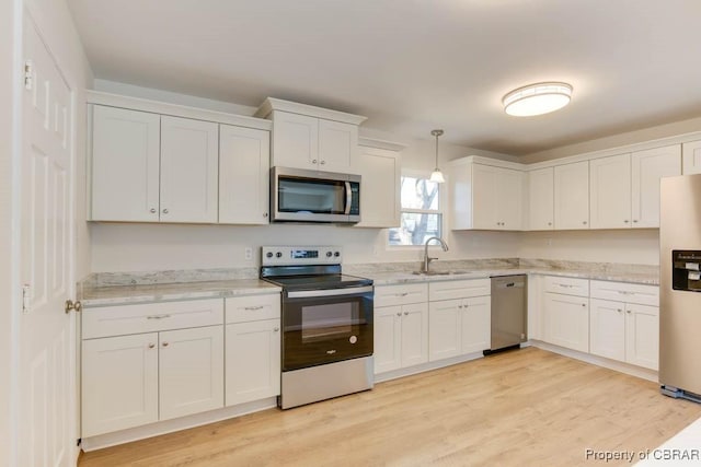 kitchen with appliances with stainless steel finishes, pendant lighting, sink, white cabinets, and light hardwood / wood-style flooring