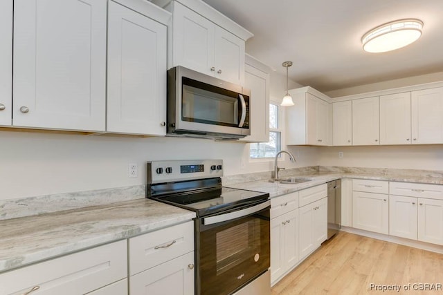 kitchen featuring pendant lighting, sink, light hardwood / wood-style flooring, stainless steel appliances, and white cabinets