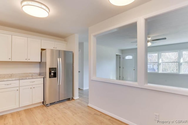 kitchen featuring white cabinets, stainless steel fridge, ceiling fan, light stone counters, and light hardwood / wood-style flooring