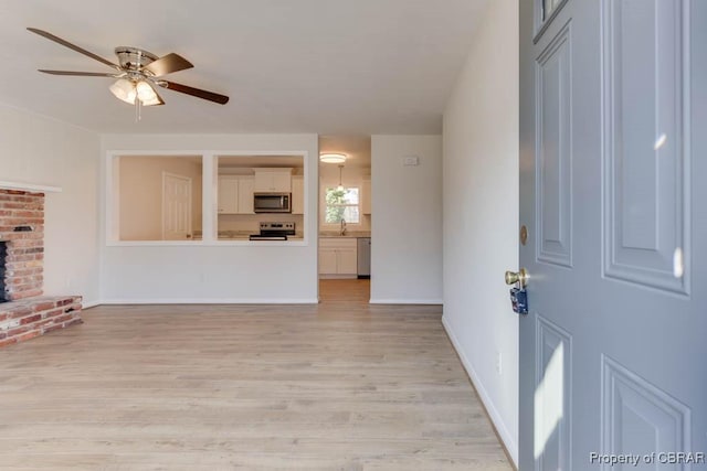 unfurnished living room with ceiling fan, sink, a fireplace, and light wood-type flooring