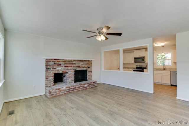 unfurnished living room with light hardwood / wood-style flooring, sink, a fireplace, and ceiling fan