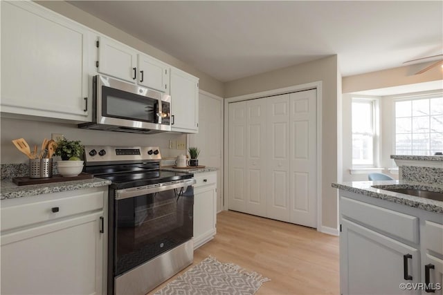 kitchen with white cabinetry, appliances with stainless steel finishes, light stone counters, and light hardwood / wood-style flooring