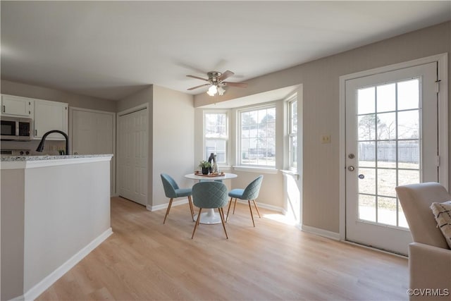 dining space with ceiling fan, sink, and light wood-type flooring