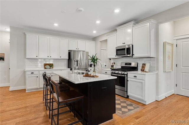 kitchen with stainless steel appliances, a kitchen breakfast bar, an island with sink, and white cabinets