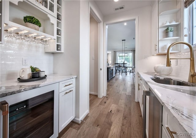 bar with tasteful backsplash, sink, white cabinets, light stone countertops, and light wood-type flooring