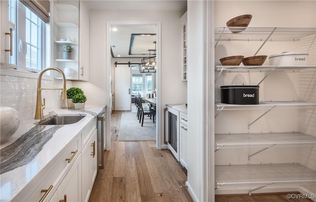 kitchen with light stone countertops, sink, white cabinets, and light hardwood / wood-style flooring