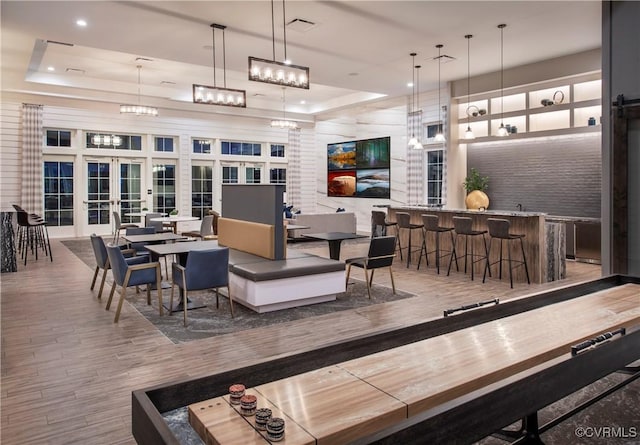 interior space featuring wood-type flooring, a high ceiling, bar, a tray ceiling, and french doors