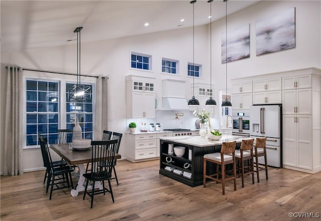 kitchen with pendant lighting, white appliances, white cabinetry, a kitchen island, and custom exhaust hood