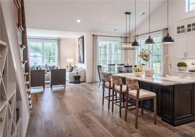 kitchen with sink, a kitchen island with sink, hanging light fixtures, light stone countertops, and white cabinets