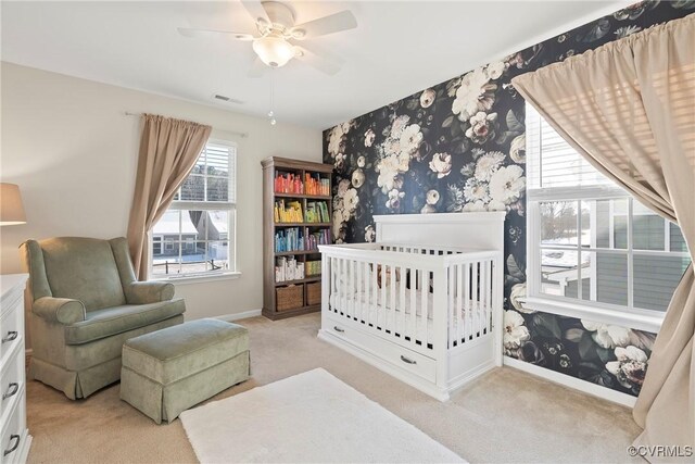 bedroom with light colored carpet, a nursery area, and ceiling fan