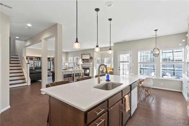 kitchen with dark brown cabinetry, sink, hanging light fixtures, dark hardwood / wood-style floors, and an island with sink