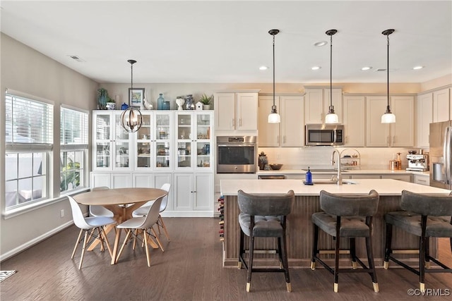 kitchen with stainless steel appliances, dark hardwood / wood-style floors, hanging light fixtures, and a center island with sink