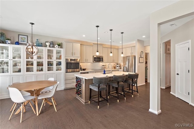 kitchen with stainless steel appliances, a kitchen breakfast bar, hanging light fixtures, and a center island with sink