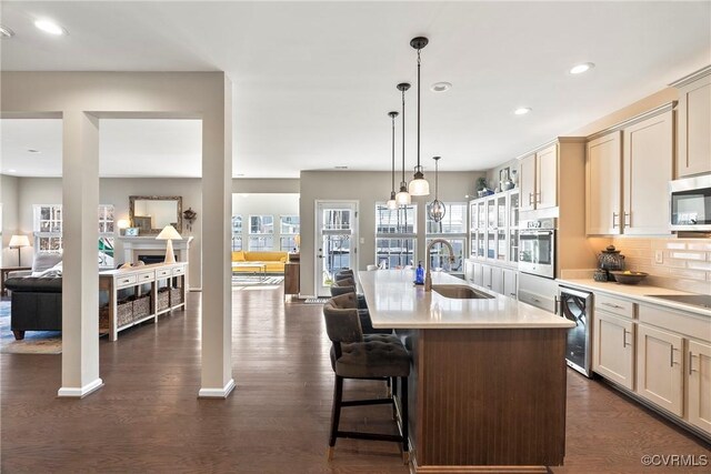 kitchen featuring appliances with stainless steel finishes, decorative light fixtures, sink, beverage cooler, and a kitchen island with sink