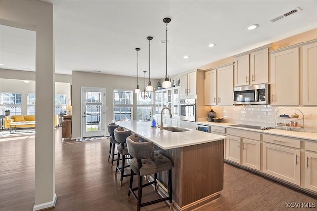 kitchen featuring appliances with stainless steel finishes, decorative light fixtures, an island with sink, sink, and a breakfast bar area