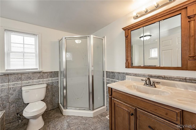 bathroom with vanity, toilet, a shower with door, and tile walls