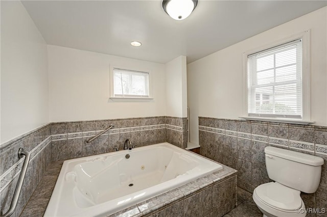 bathroom with tile walls, tiled tub, and toilet