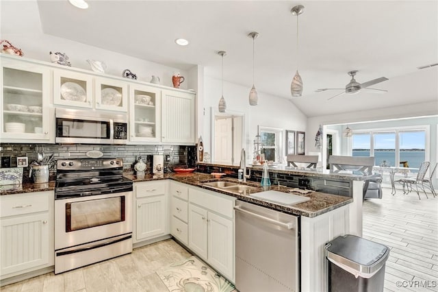 kitchen featuring appliances with stainless steel finishes, pendant lighting, white cabinets, dark stone counters, and a water view