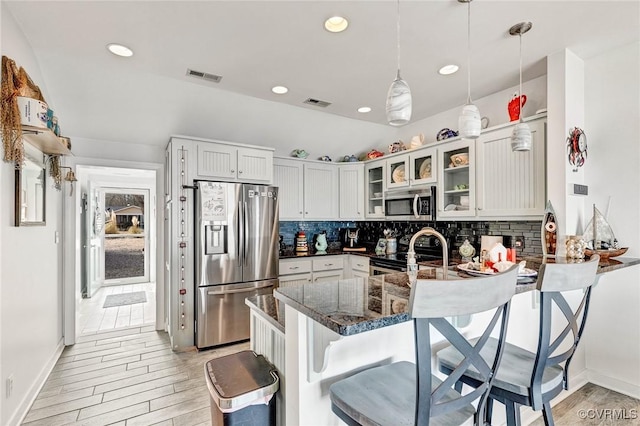 kitchen with appliances with stainless steel finishes, dark stone countertops, a breakfast bar area, hanging light fixtures, and kitchen peninsula