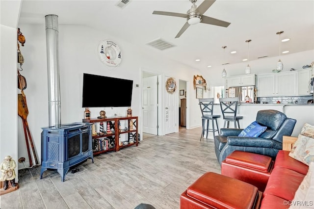 living room featuring ceiling fan, lofted ceiling, a wood stove, and light wood-type flooring