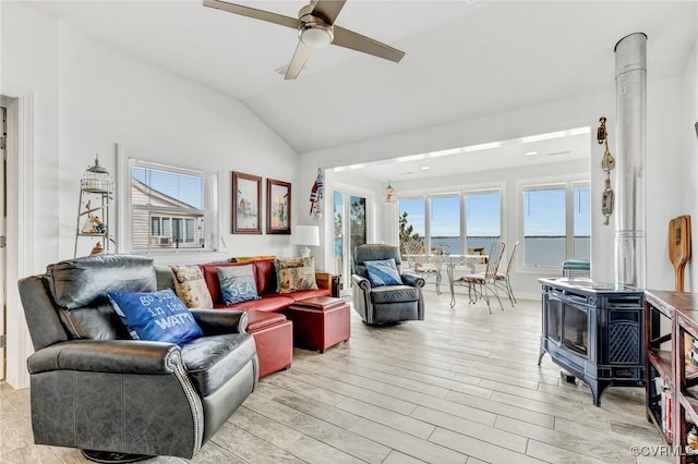 living room with vaulted ceiling, a wood stove, ceiling fan, light hardwood / wood-style floors, and a water view