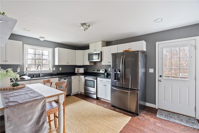 kitchen with appliances with stainless steel finishes, sink, wood-type flooring, and white cabinets