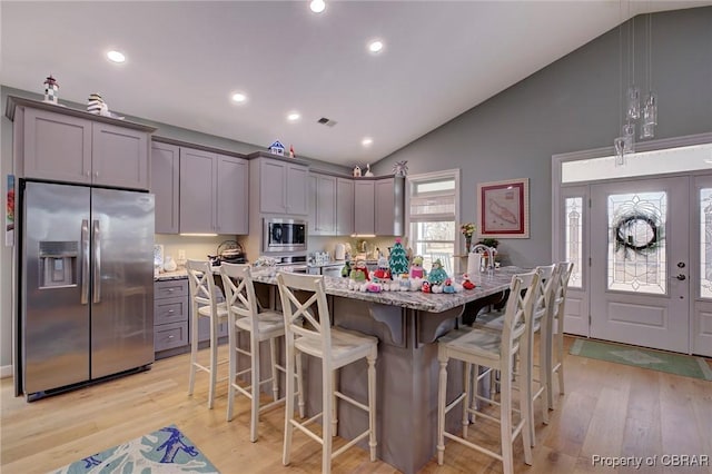 kitchen featuring stainless steel appliances, decorative light fixtures, gray cabinets, and a center island with sink