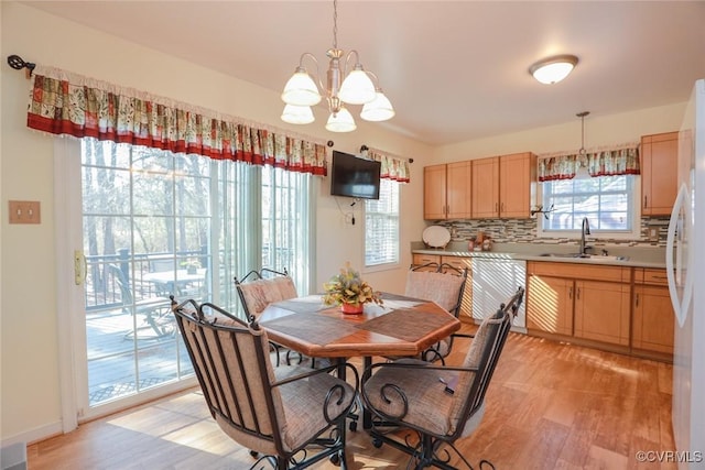 dining space featuring a healthy amount of sunlight, sink, a notable chandelier, and light wood-type flooring