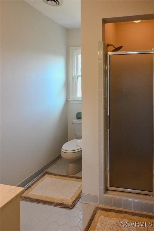 bathroom with tile patterned floors, toilet, and a shower with shower door