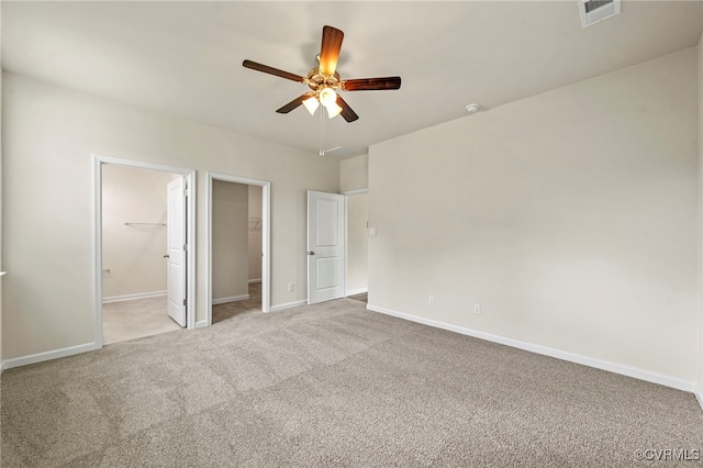 unfurnished bedroom featuring ceiling fan, ensuite bathroom, a spacious closet, light colored carpet, and a closet