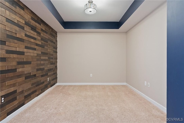 unfurnished room with a tray ceiling, light carpet, and wood walls