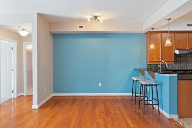 kitchen with a breakfast bar area, decorative backsplash, hanging light fixtures, kitchen peninsula, and light wood-type flooring