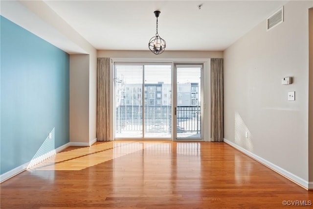 unfurnished room featuring an inviting chandelier and light hardwood / wood-style flooring