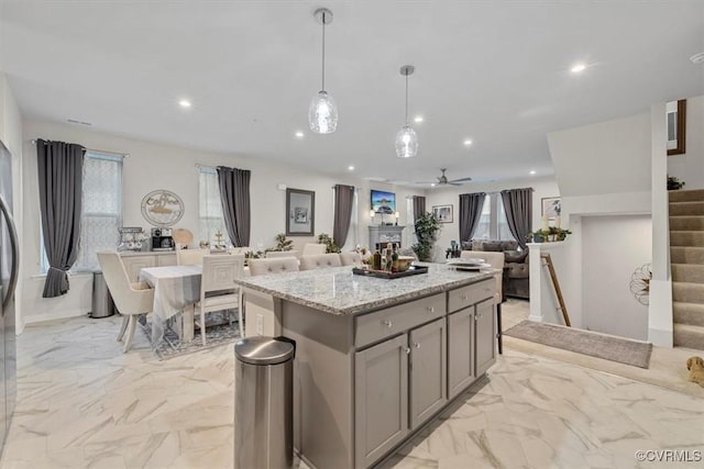 kitchen with decorative light fixtures, gray cabinets, a kitchen island, ceiling fan, and light stone countertops