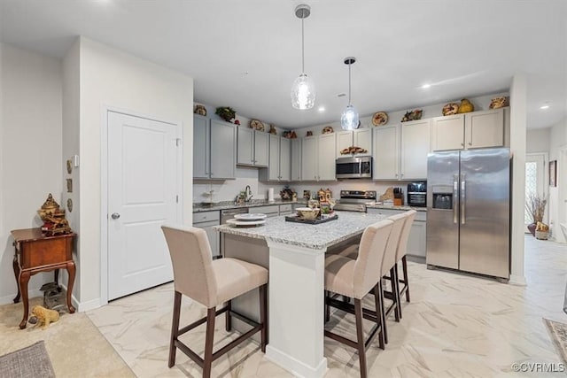 kitchen featuring gray cabinetry, hanging light fixtures, stainless steel appliances, a kitchen breakfast bar, and a kitchen island